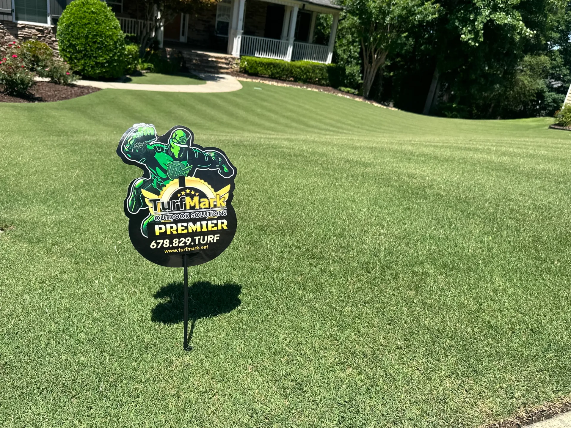 A TurfMark Premier yard sign on a thick striped lawn in front of a house