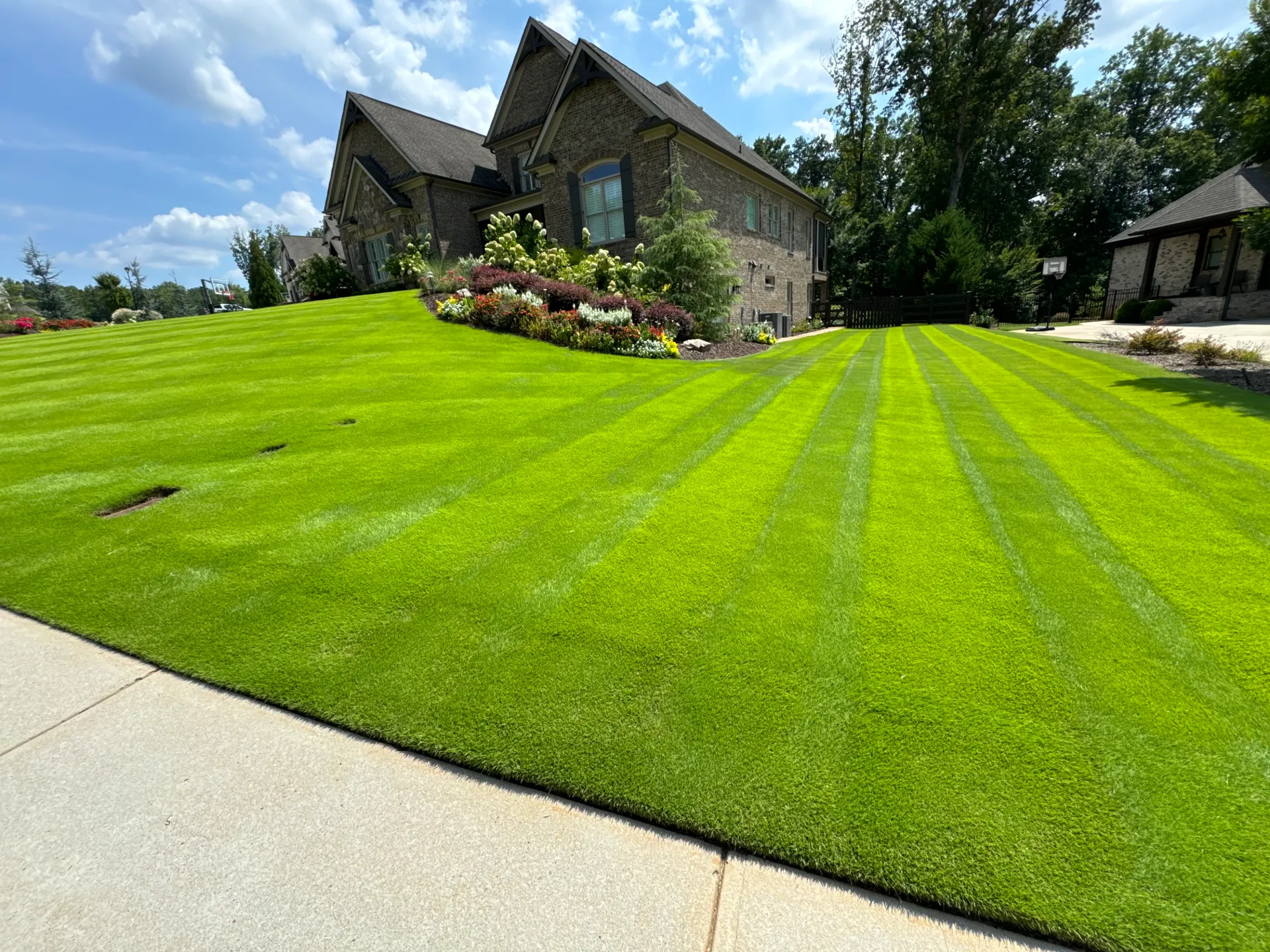A thick, freshly striped lawn in front of a stone house with a landscaped island bed