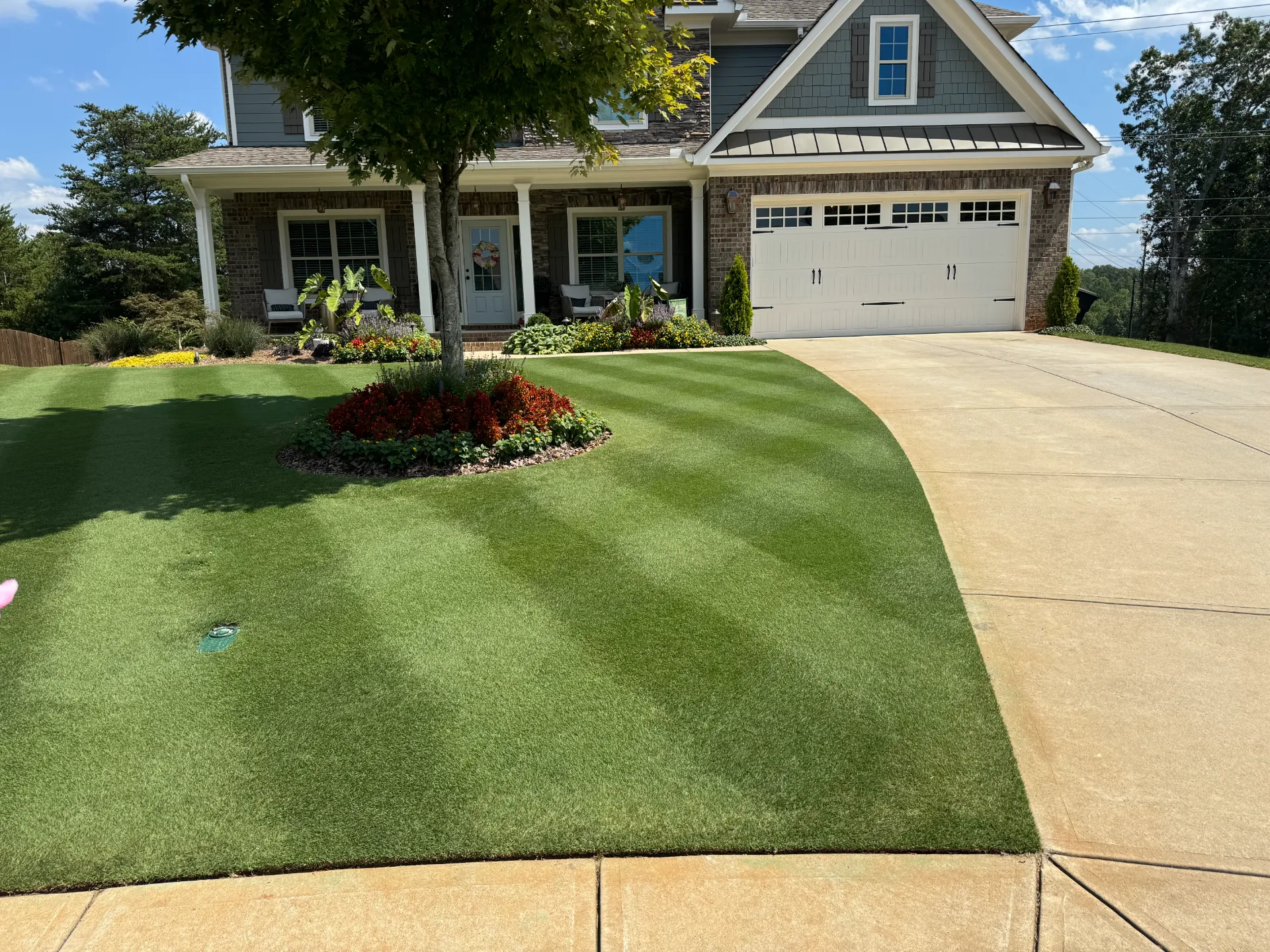 A striped front lawn curving along the driveway of a two-story house with a front porch