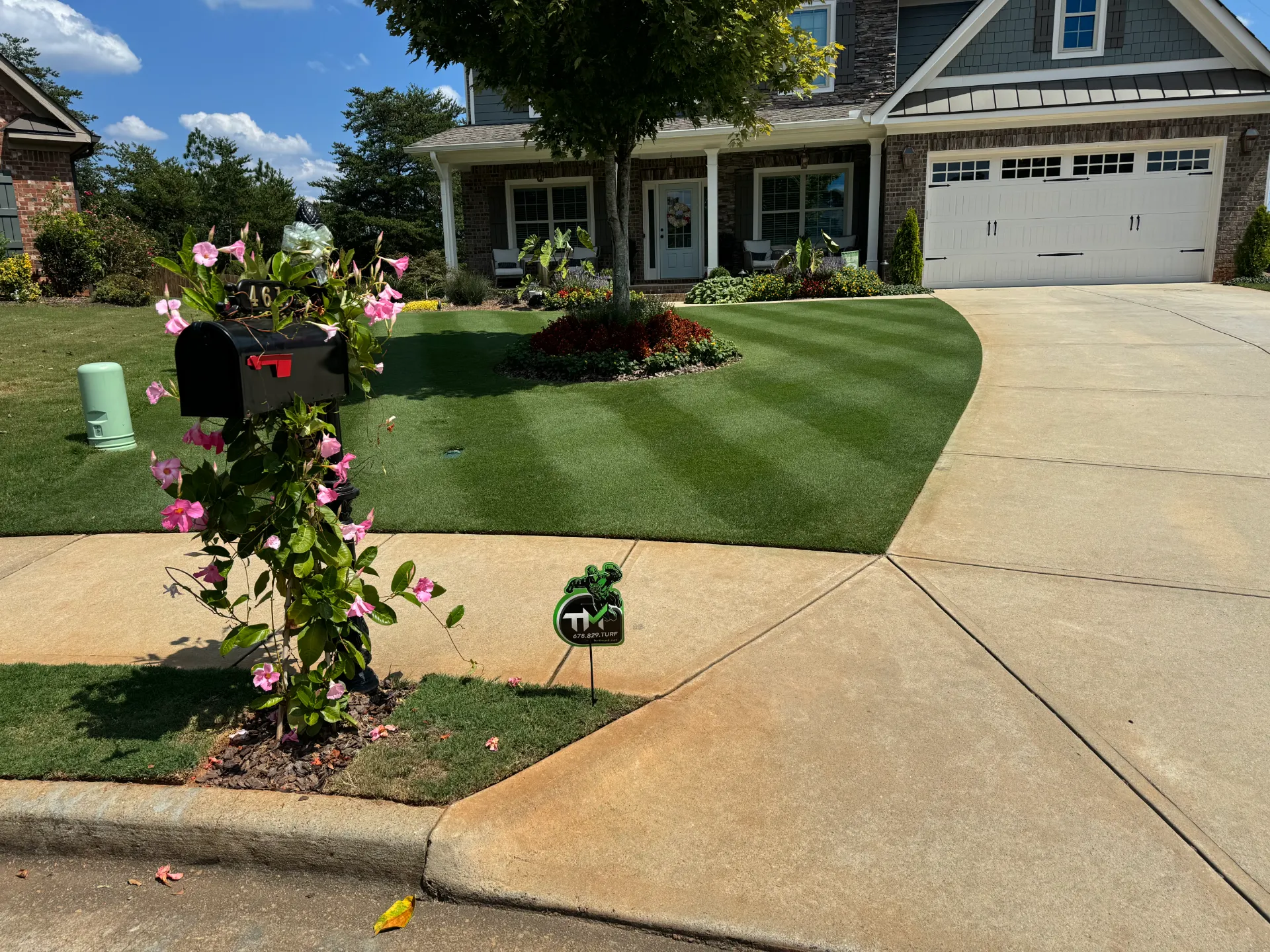 A striped front lawn with a flowering mailbox and a small TurfMark sign by the driveway