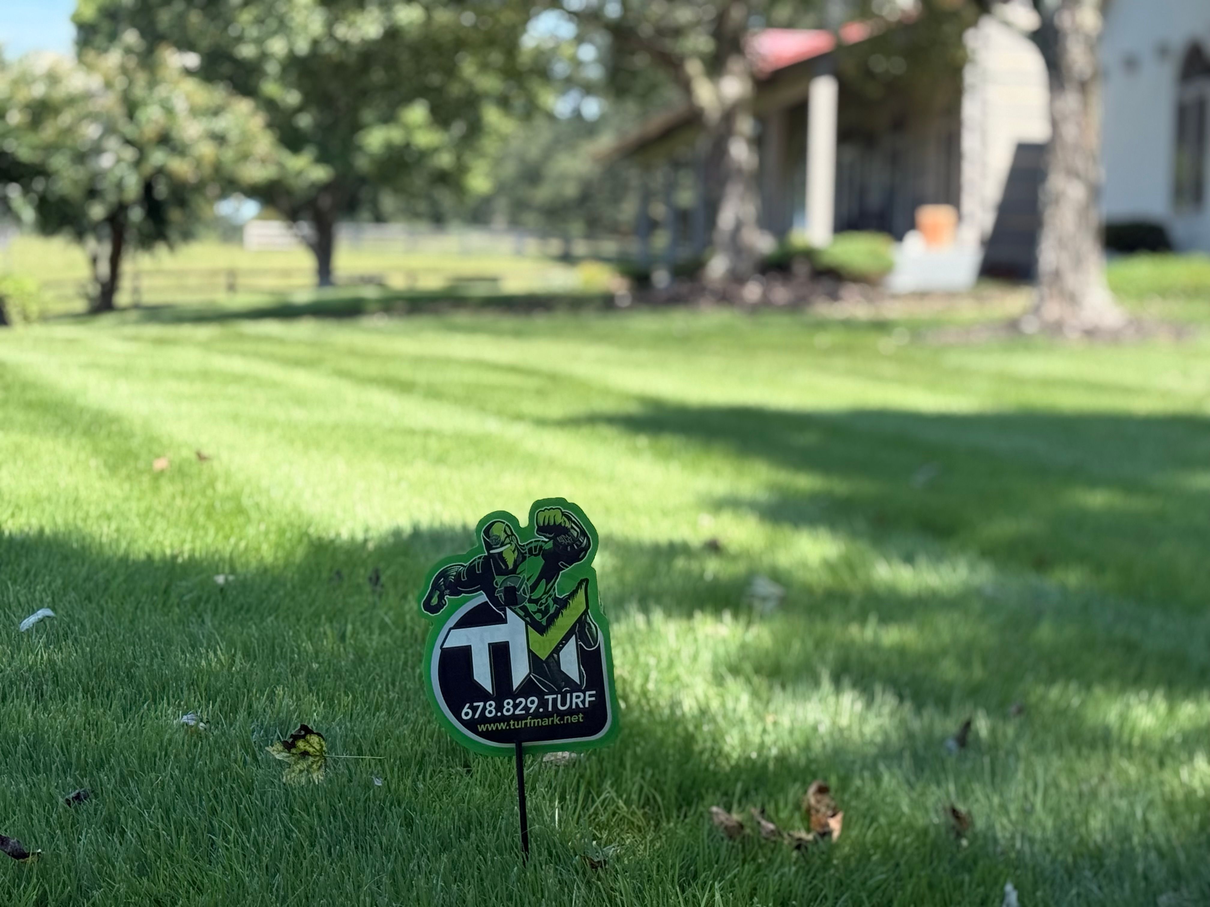 A TurfMark yard sign on a striped lawn under tall shade trees