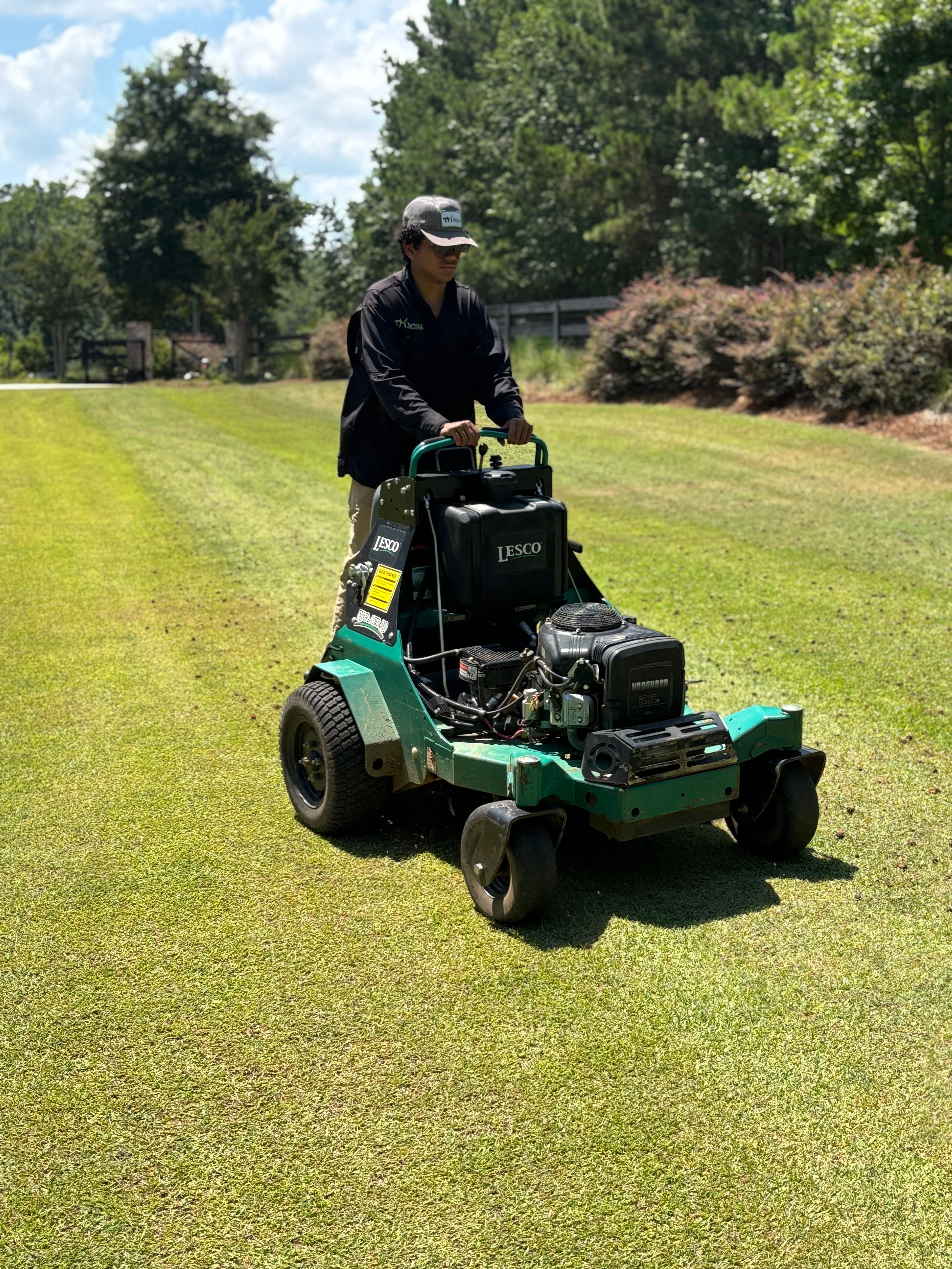 A TurfMark technician running a core aerator across a lawn