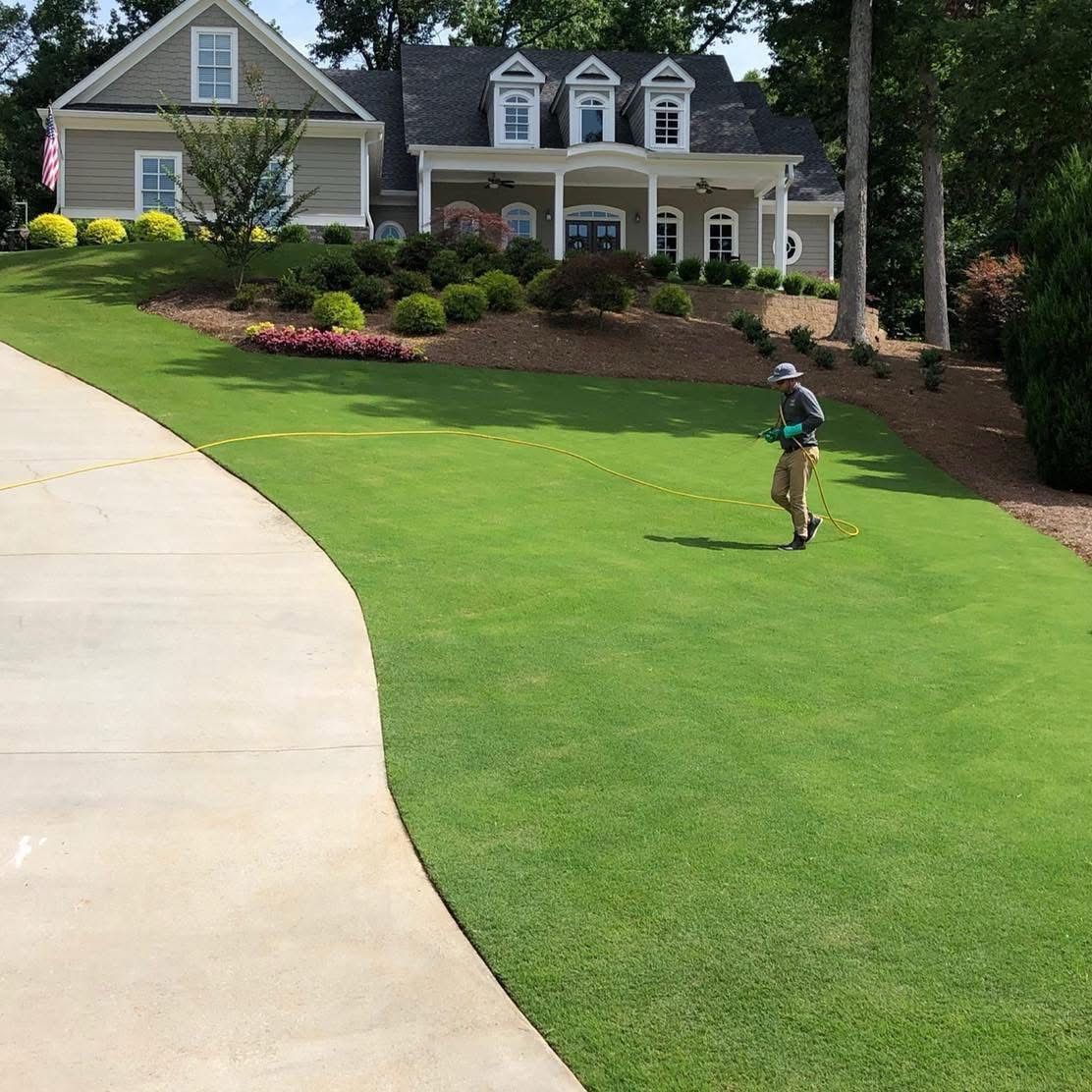 A TurfMark technician treating a large green lawn beside a curving front walk