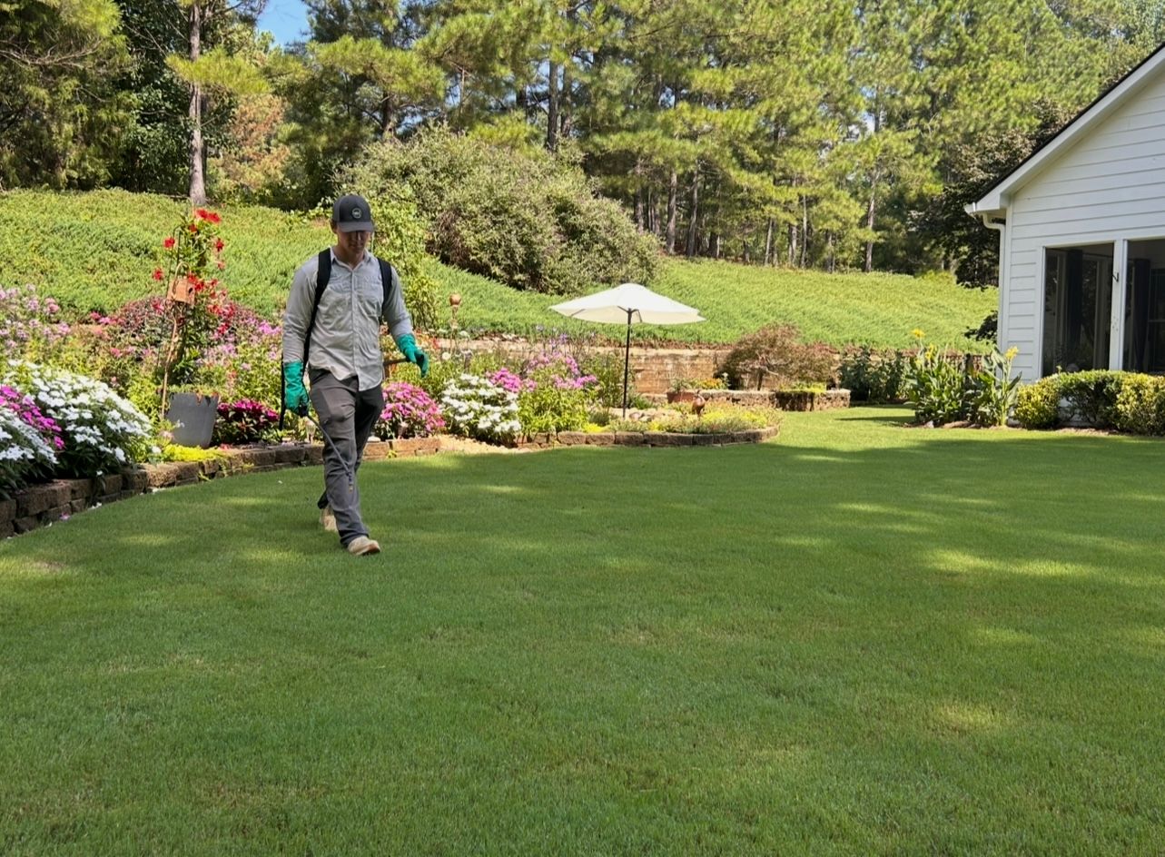 A TurfMark technician treating a backyard lawn beside flower beds and a patio umbrella