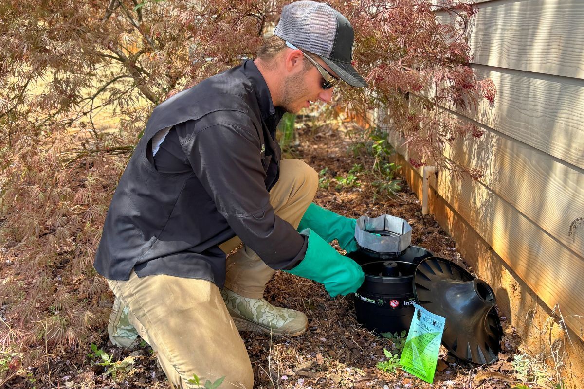 A TurfMark technician setting an In2Care mosquito station beside a house